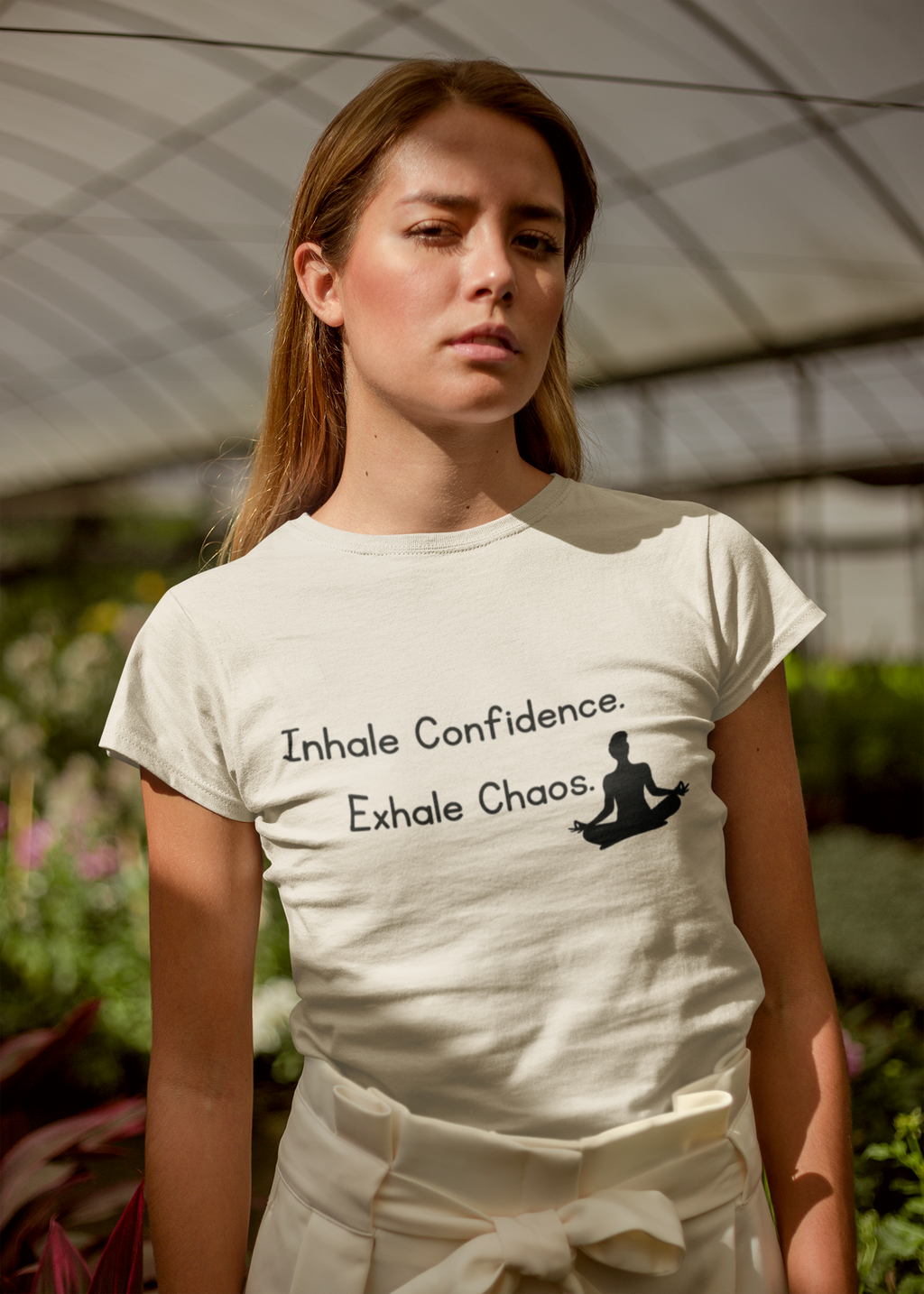 A woman wearing a cream-colored t-shirt with the black printed text 'Inhale Confidence. Exhale Chaos.