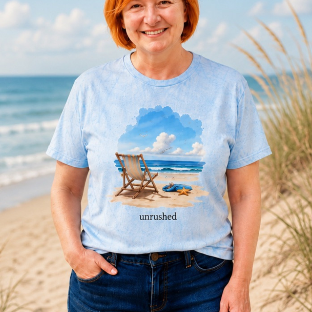 Person wearing a light blue t-shirt with a beach scene and 'unrushed' text on a sandy beach.