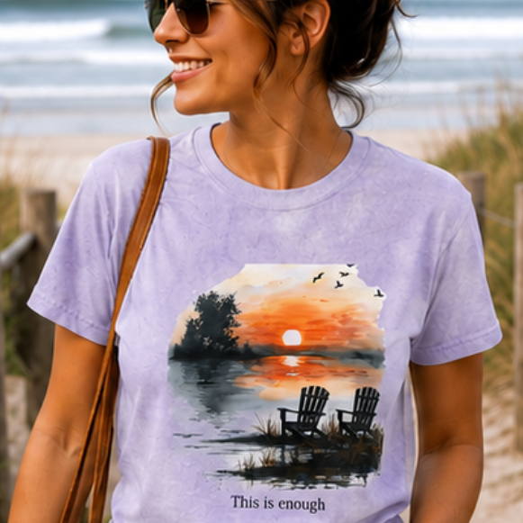 Woman wearing a purple t-shirt with a sunset design on a beach.