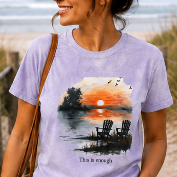 Woman wearing a purple t-shirt with a sunset design on a beach.