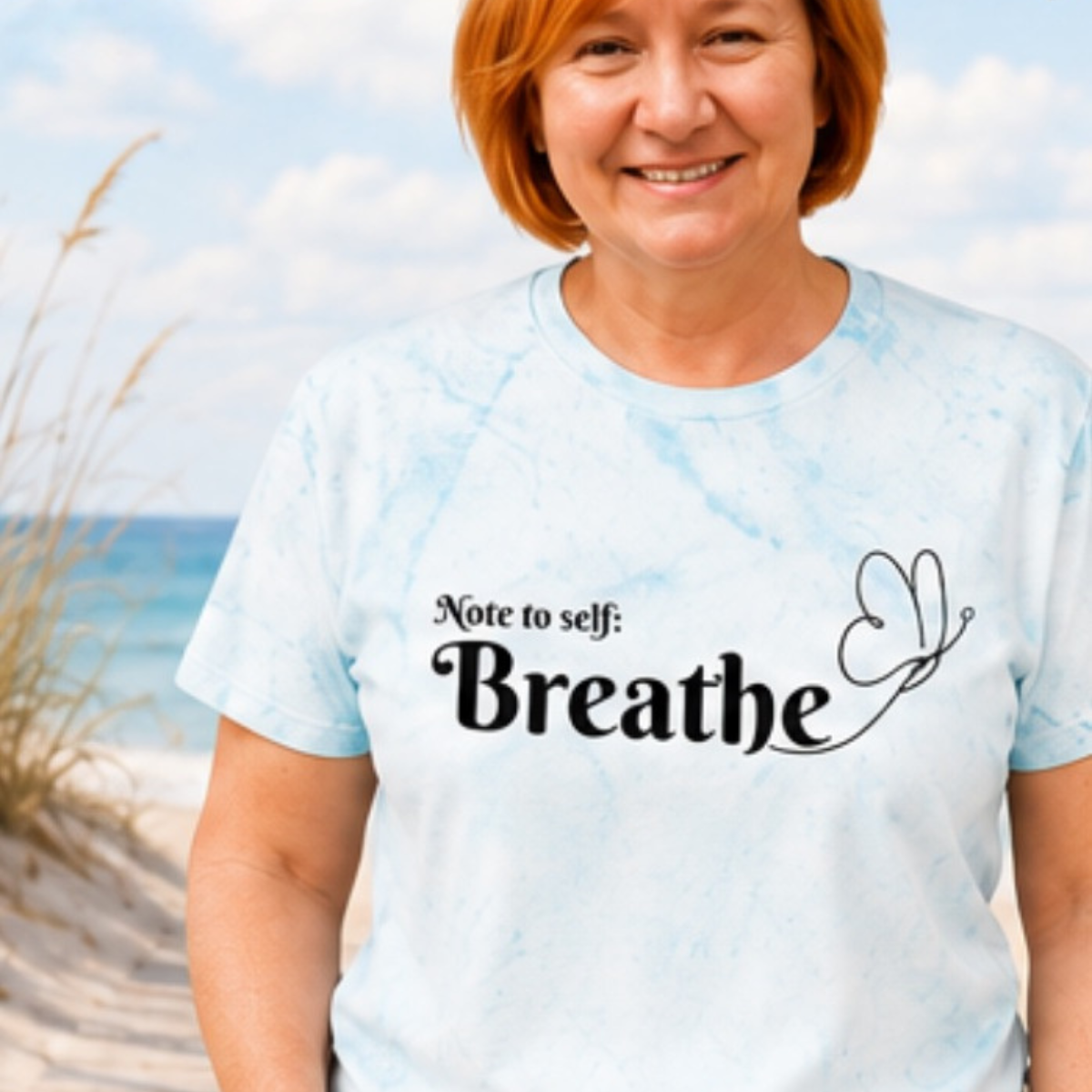 Woman wearing a light blue t-shirt with 'Note to self: Breathe' text on a beach.