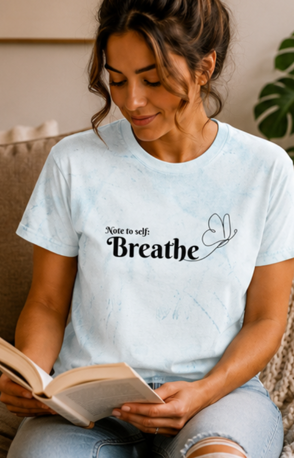 Woman reading a book and holding a coffee mug, wearing a t-shirt with 'Breathe' text.