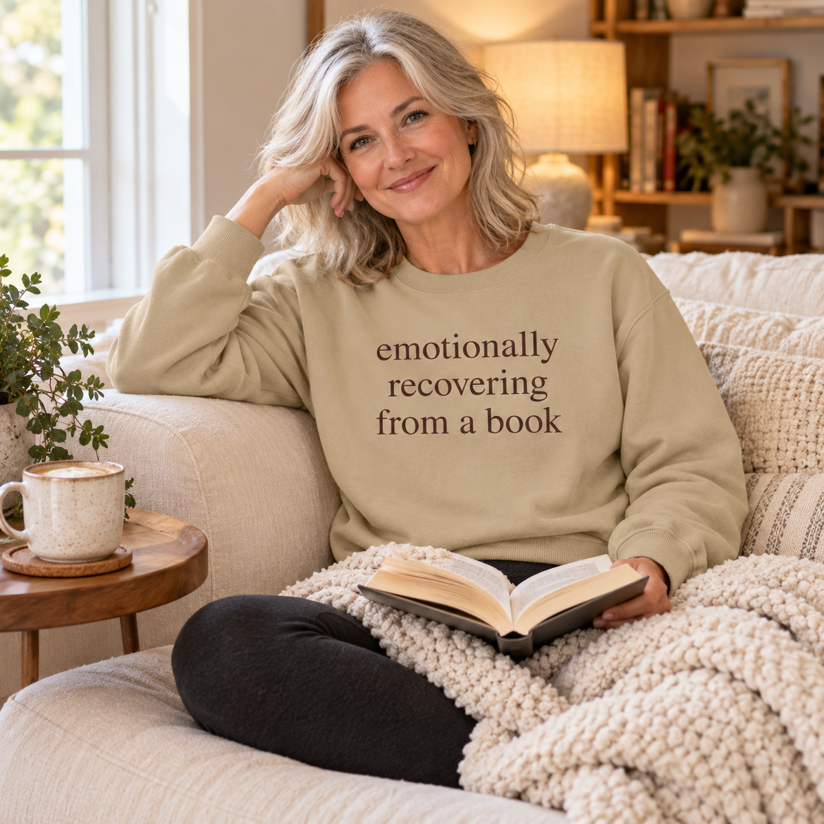 Sand sweatshirt. Size S-3XL, Woman relaxing on a couch with her favorite book wearing the Emotionally recovering from a Book crewneck sweatshirt.